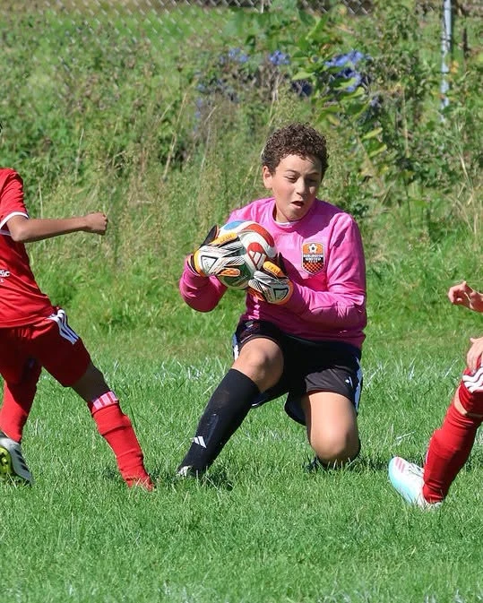 A BUSC 11U Boys Orange goalkeeper holding the ball during a match.