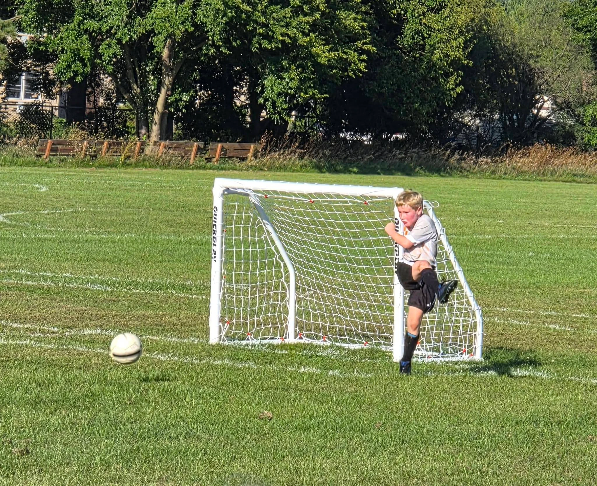 A BUSC 8U Boys Orange player kicking the ball away from a small soccer goal.