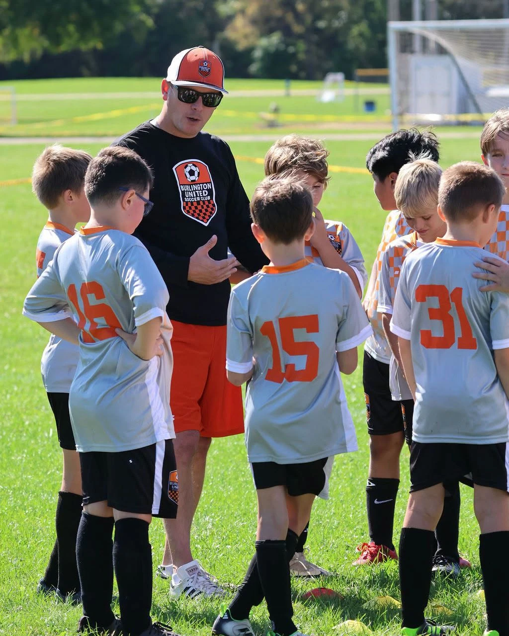 A BUSC coach talking with 11U Boys Orange players in a team huddle.