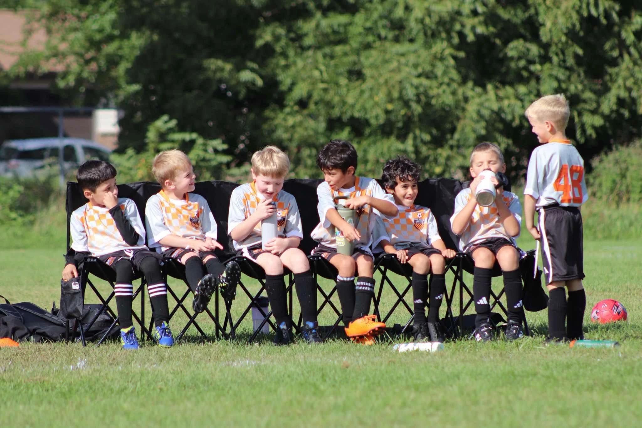 BUSC 8U Boys Orange players sitting together on the sideline during a match.